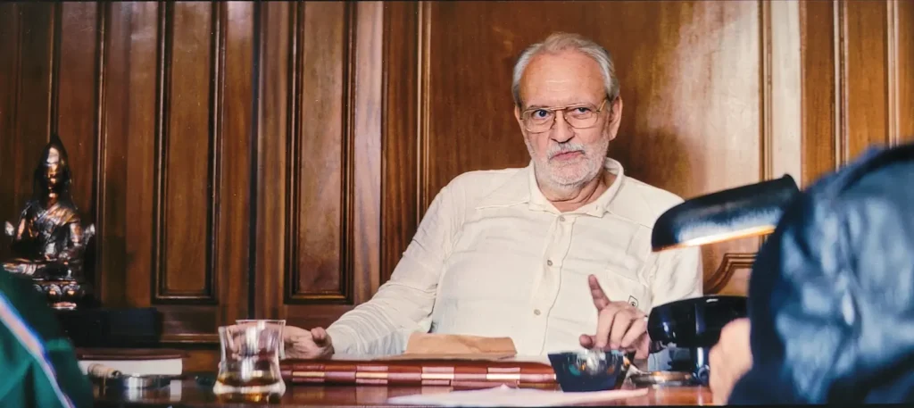 Personagem do ator Luciano Chirolli em "O Agente Secreto", um empresário, bebendo whisky em seu escritório (Reprodução)