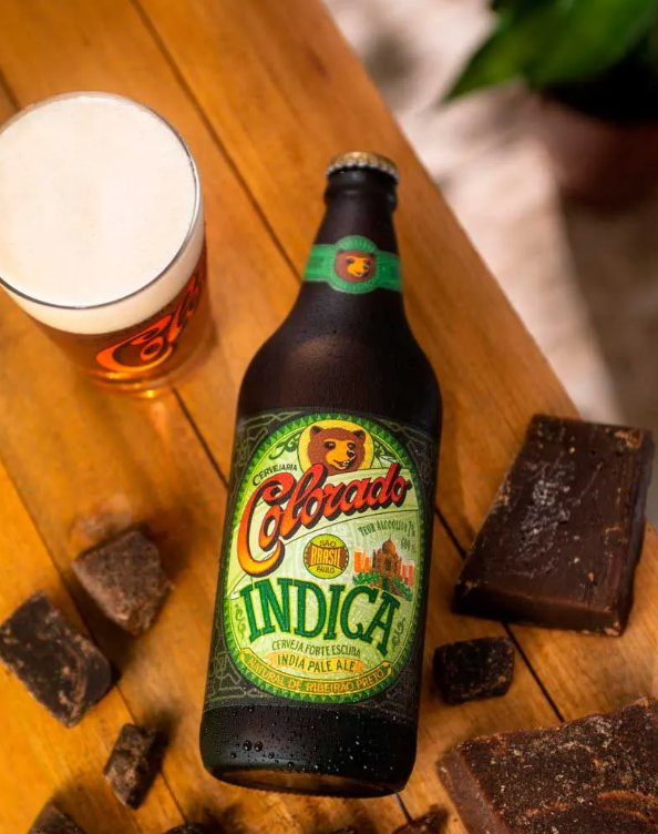 Garrafa de Colorado Indica, India Pale Ale de Ribeirão Preto, ao lado de copo de cerveja e pedaços de rapadura sobre mesa de madeira